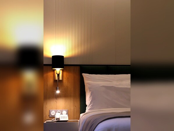 Habitación de hotel con cama, mesita de noche con lámpara e interruptor de luz en la pared.
