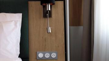 A hotel room with a bed, a wall-mounted lamp, and a thermostat control panel.