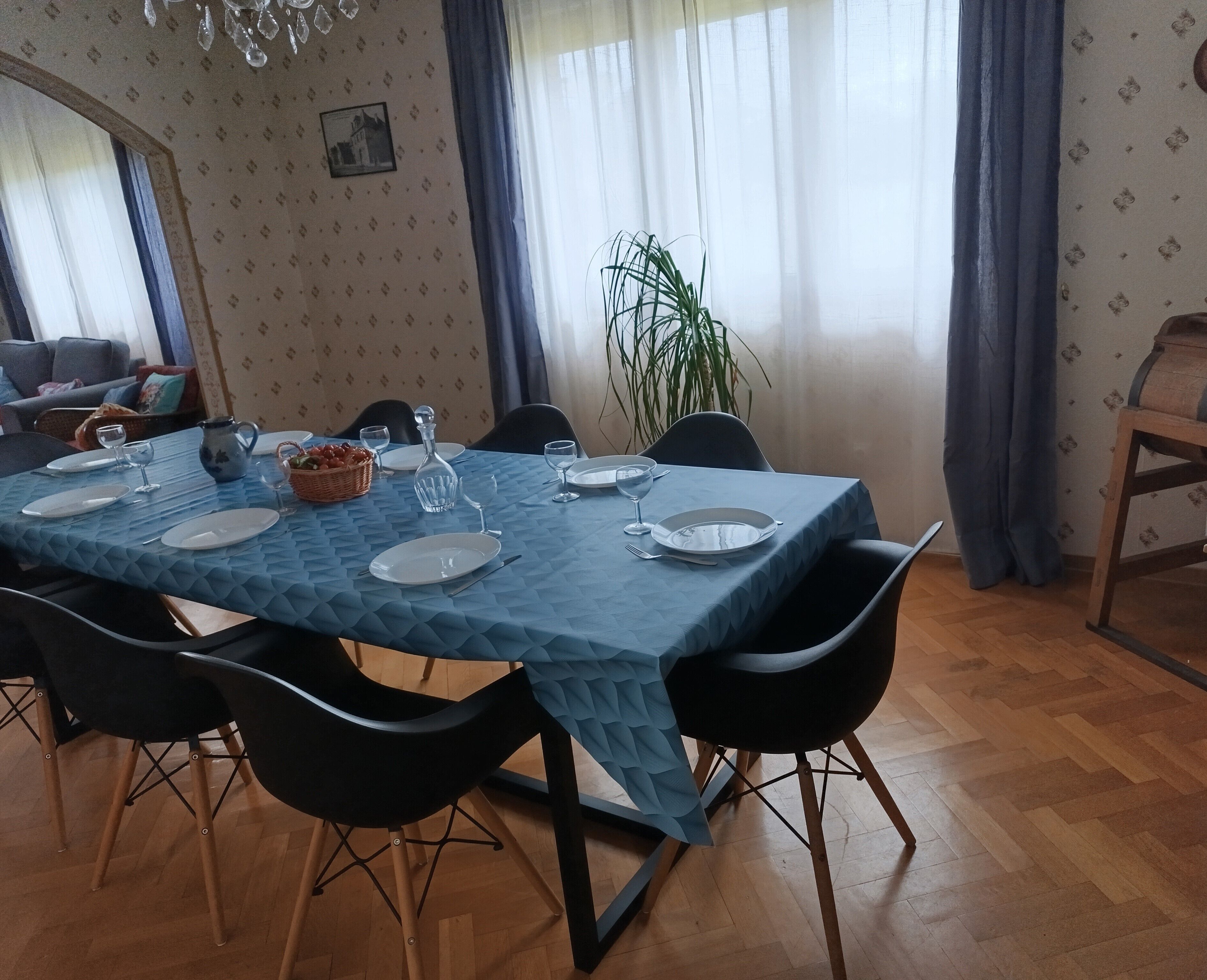 Ein Essbereich mit Tisch für vier Personen, Stühlen, einer Kronleuchter, einem Blumentopf und einer Wand mit Muster.