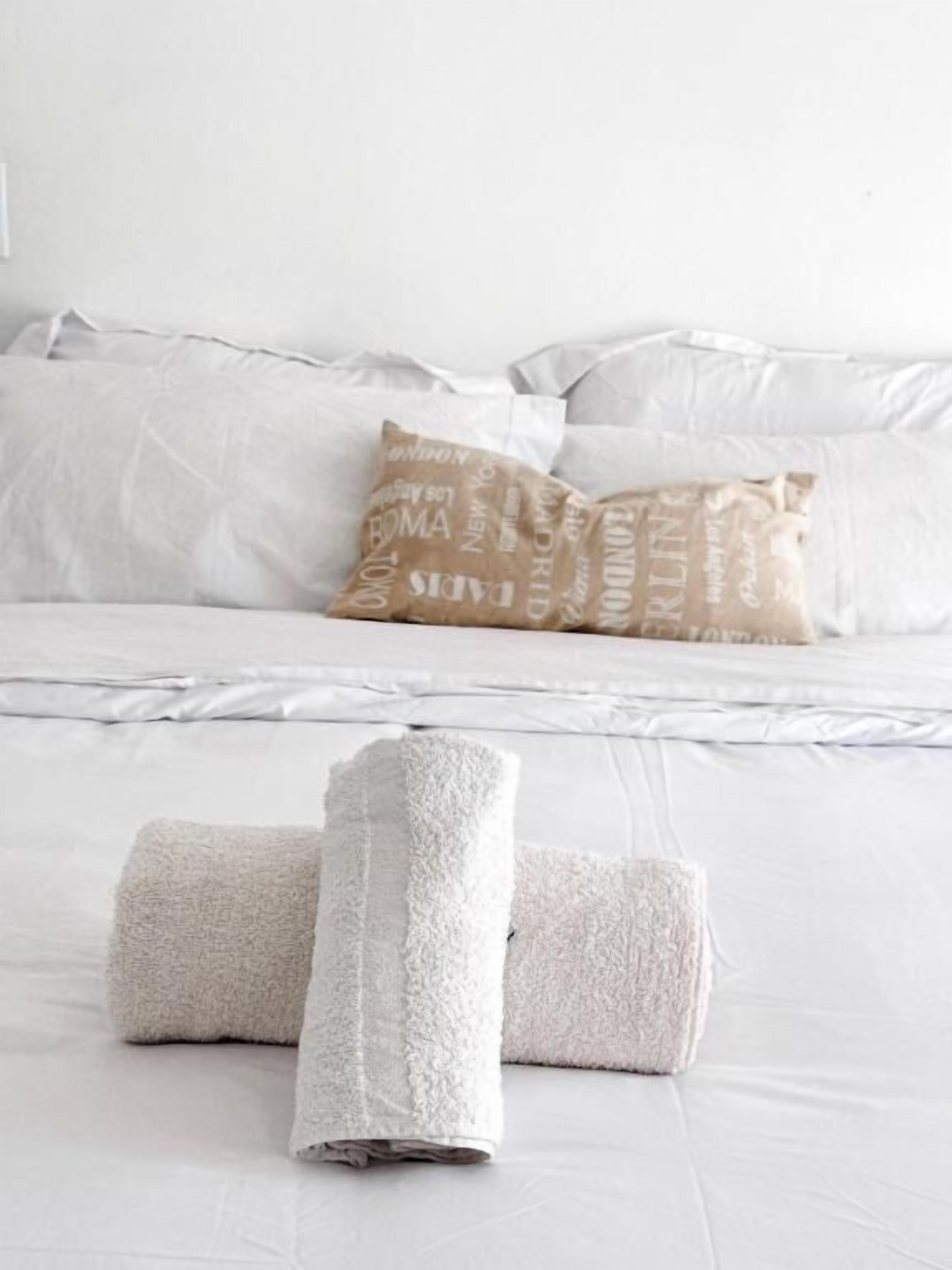 Una cama bien hecha con sábanas blancas y una sola almohada color beige con texto.