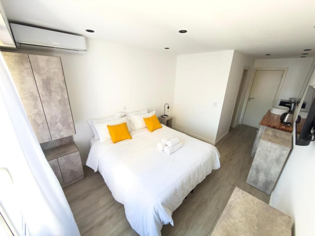 A hotel room with a bed, a nightstand, a mirror, and a wooden floor.