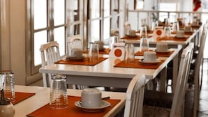 Un restaurante con varias mesas dispuestas, con platos blancos, tazas y vasos transparentes.