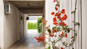 Un pasillo con techo de concreto, una pared blanca con una planta trepadora y una puerta al final.