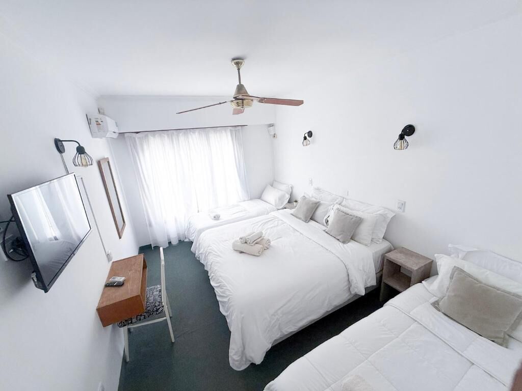 Quarto de hotel com duas camas, televisão, ventoinha no teto e uma janela com cortinas.