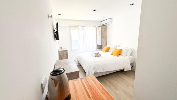 Una habitación de hotel con cama, una mesa de madera, un hervidor y una ventana con cortinas.