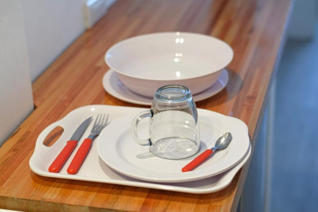 A dining setup with a white plate, a glass mug, and cutlery on a wooden table.