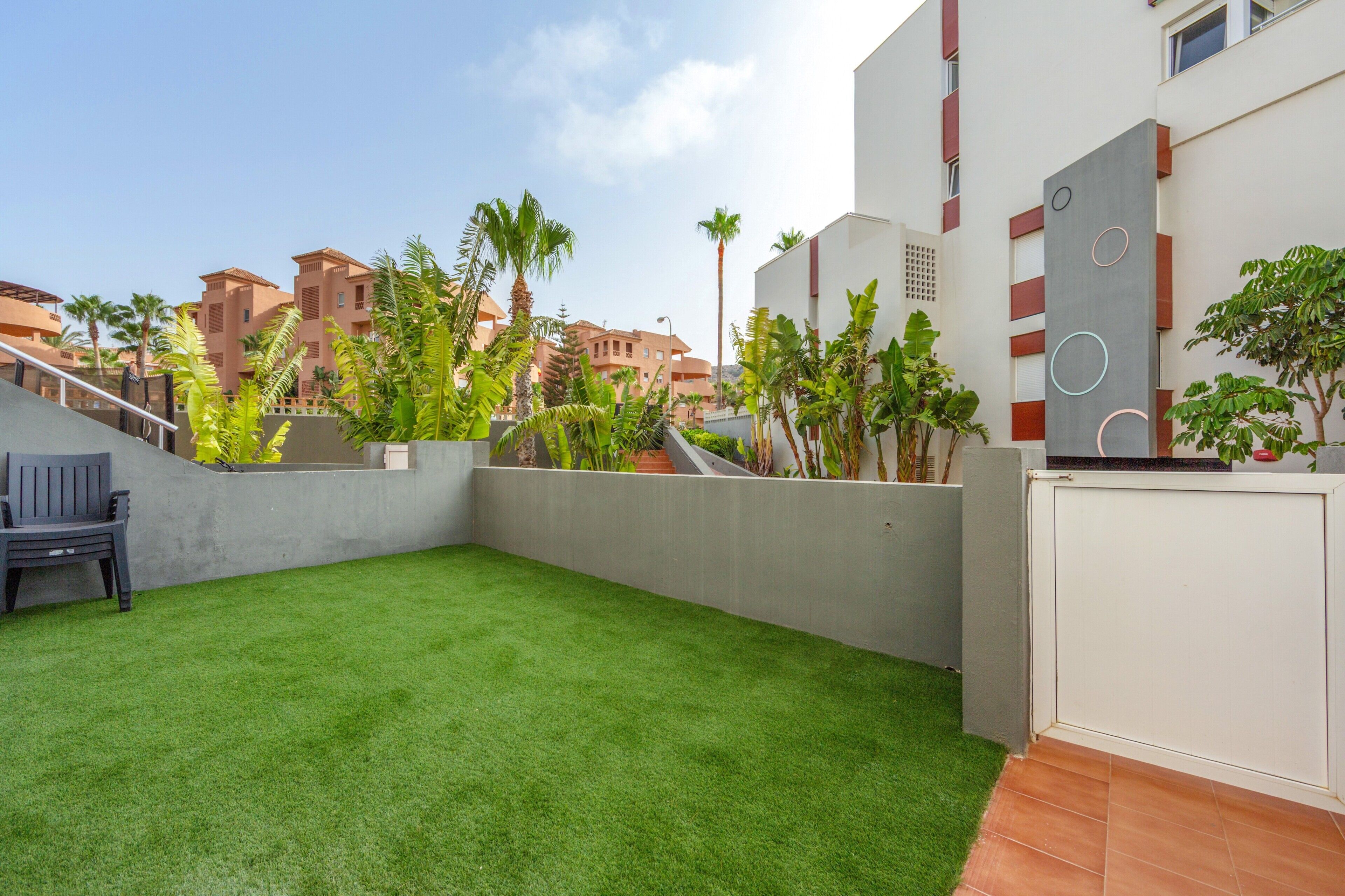 A courtyard with artificial grass, a bench, and a white wall with circular patterns.
