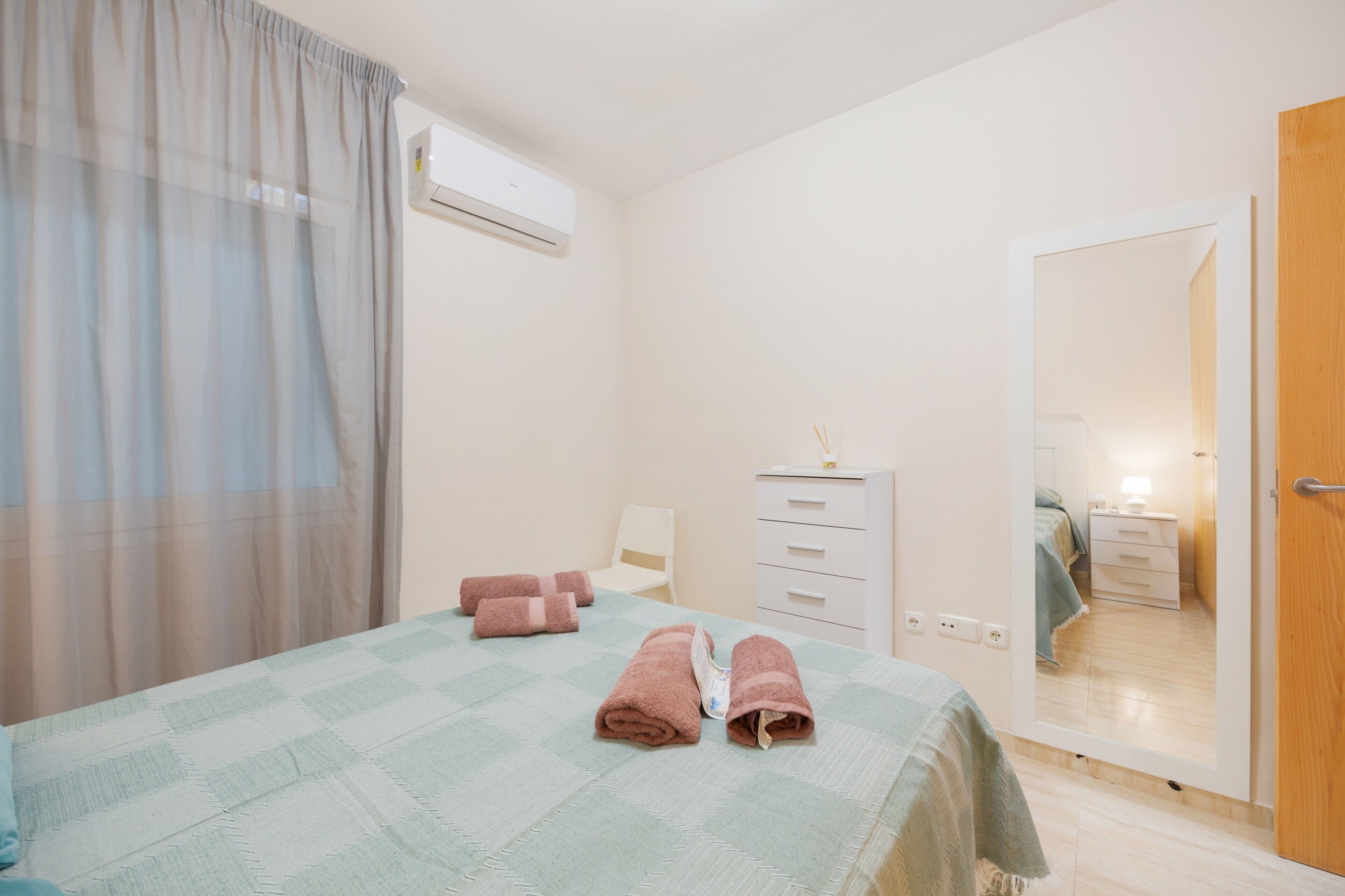Un dormitorio con cama, cómoda, espejo y aire acondicionado.