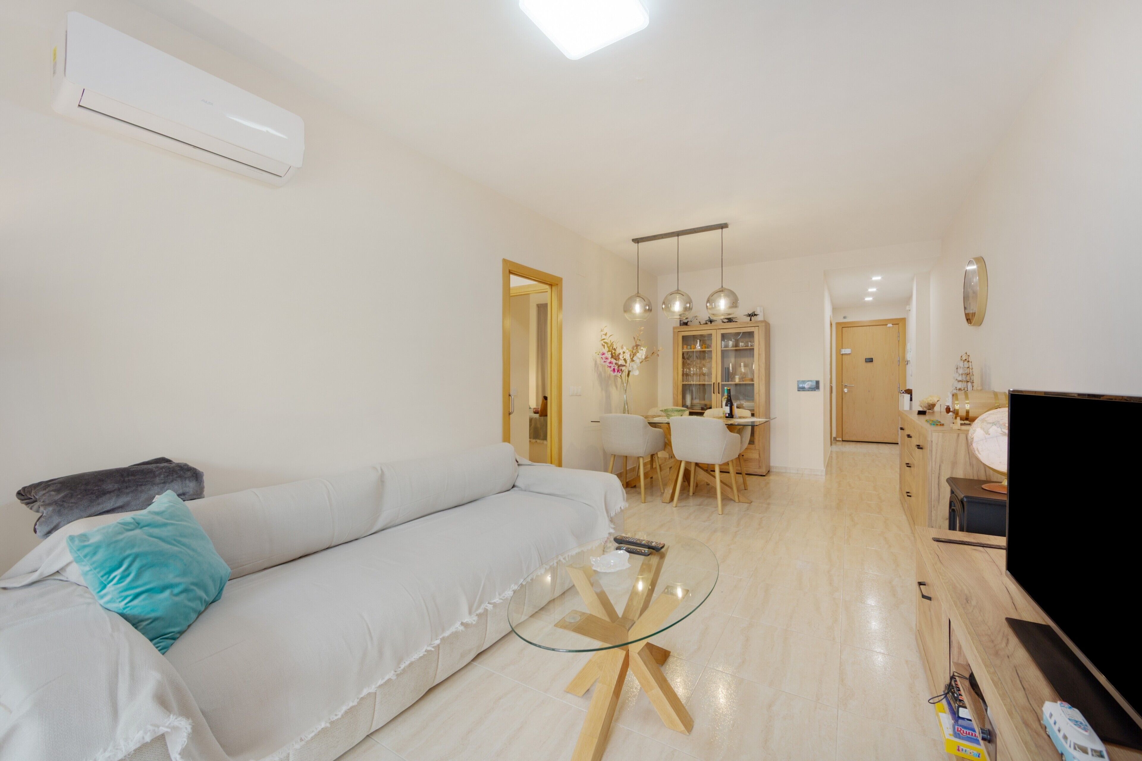 Una sala de estar moderna con un sofá blanco, una mesa de centro de vidrio y un televisor de pantalla plana.