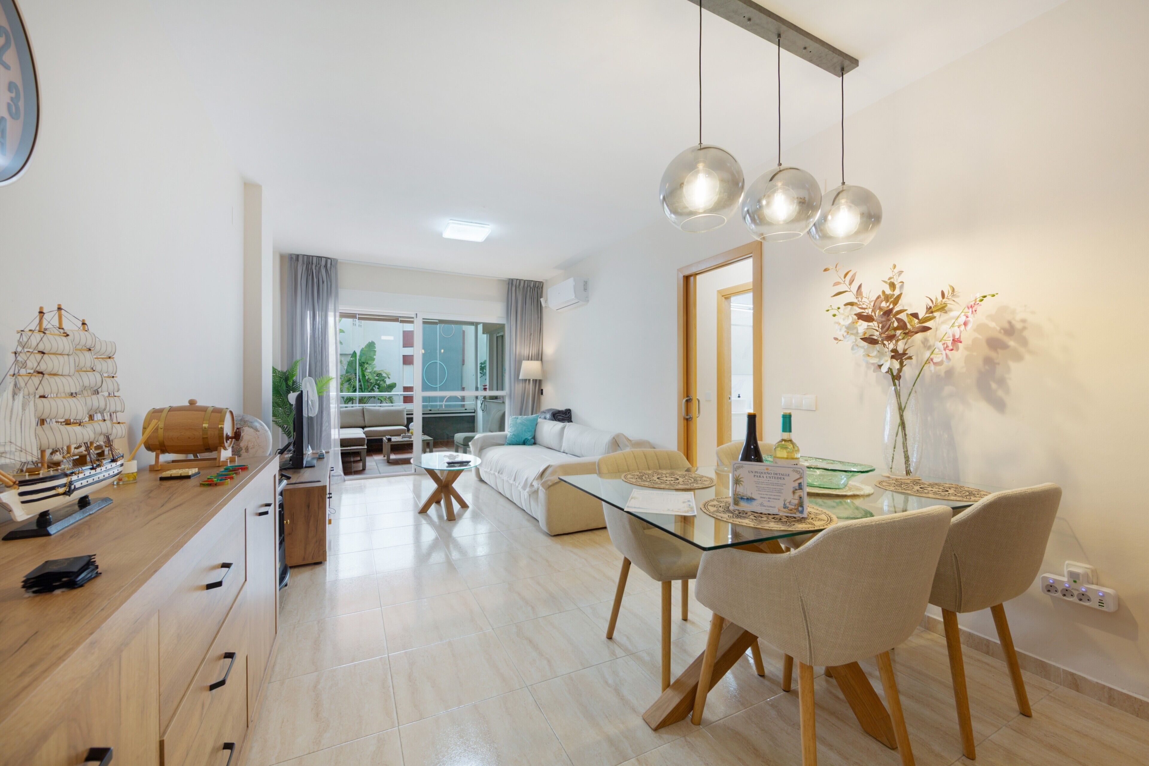 Una sala de estar moderna con una mesa de comedor de vidrio, sillas de madera y un modelo de barco en la encimera.