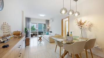 Una sala de estar moderna con una mesa de comedor de vidrio, sillas de madera y un modelo de barco en la encimera.