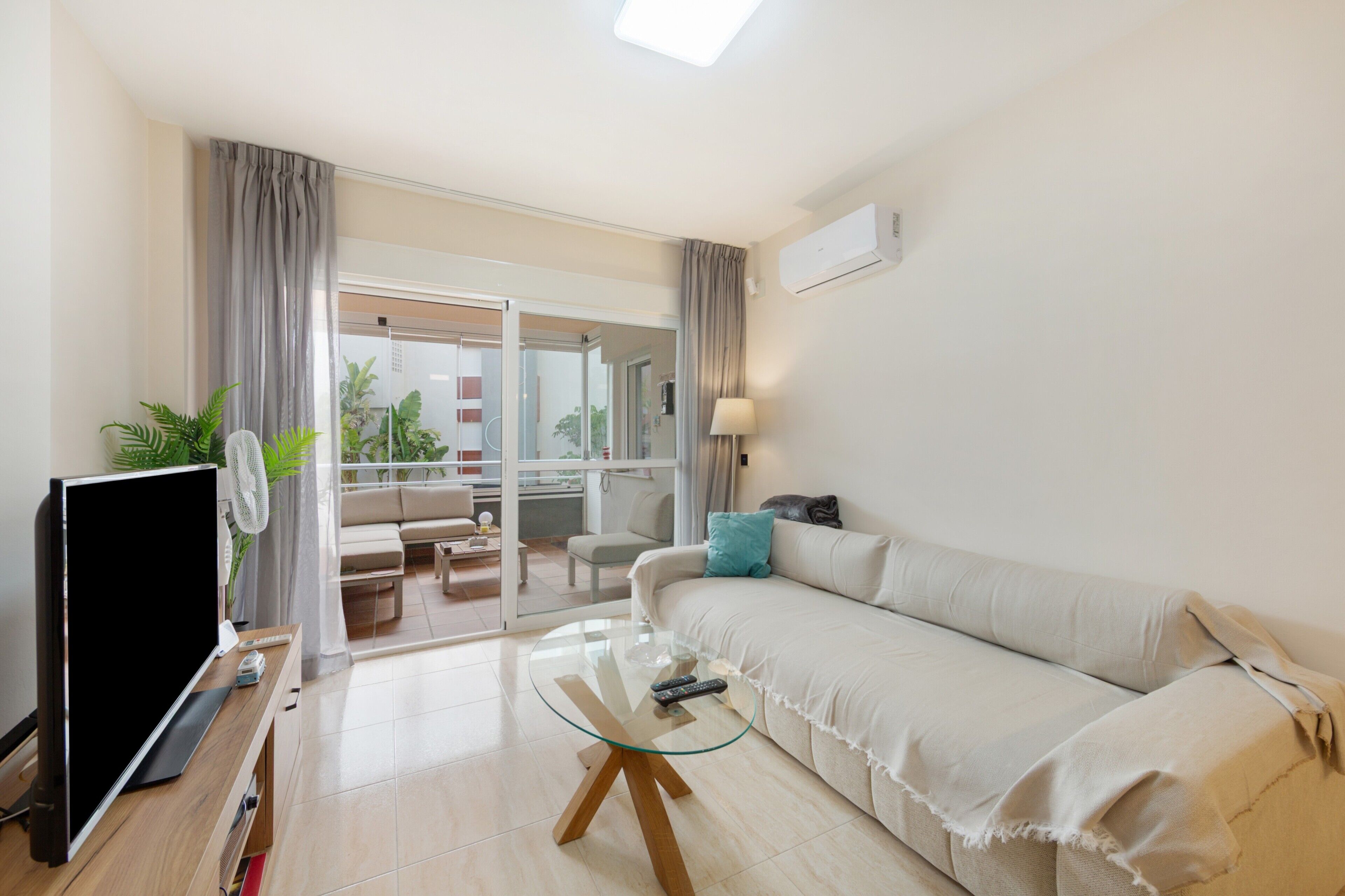 Una sala de estar moderna con televisor de pantalla plana, mesa de centro de vidrio, sofá y un balcón con puertas correderas.