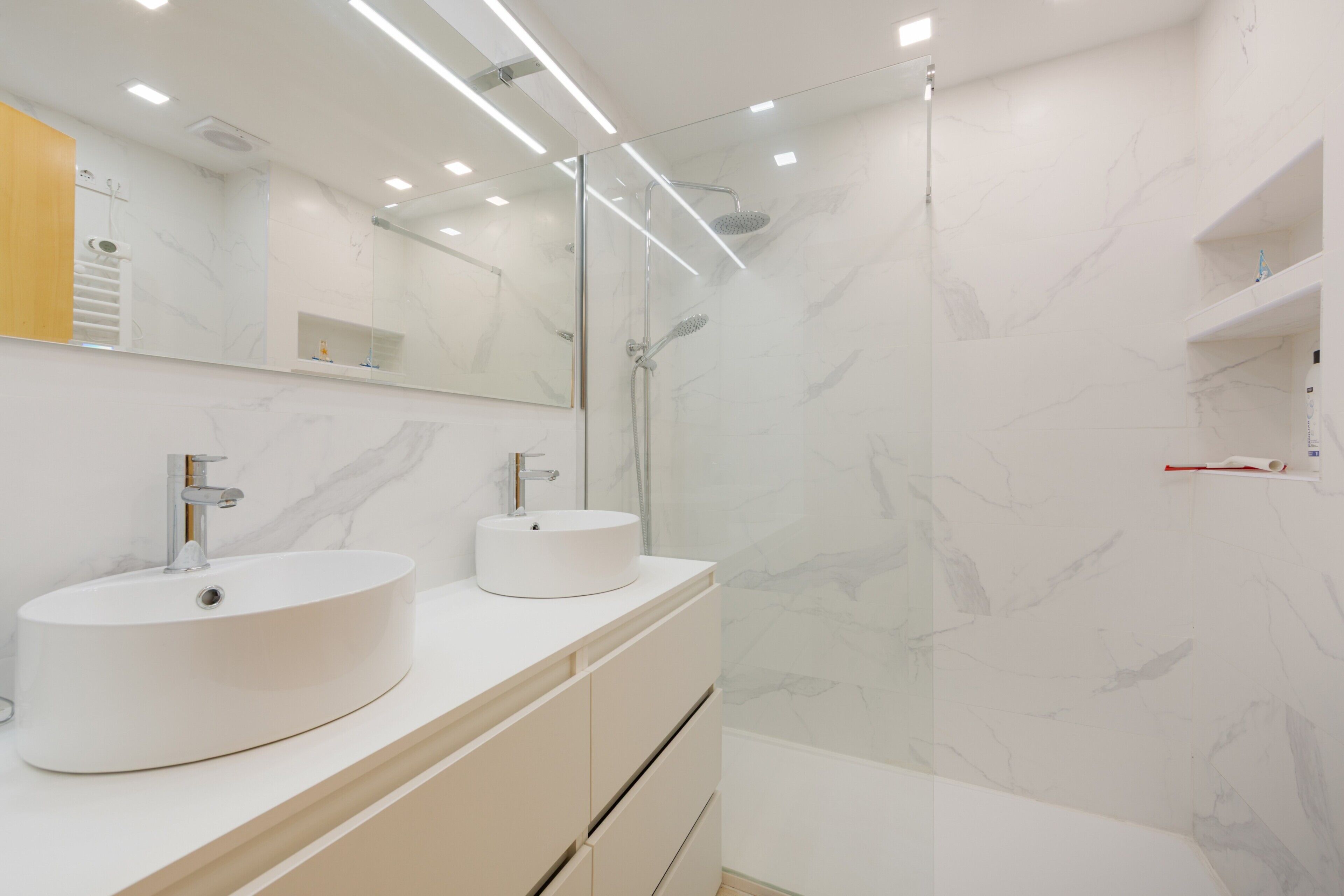 Un baño moderno con dos lavamanos, ducha y espejo.