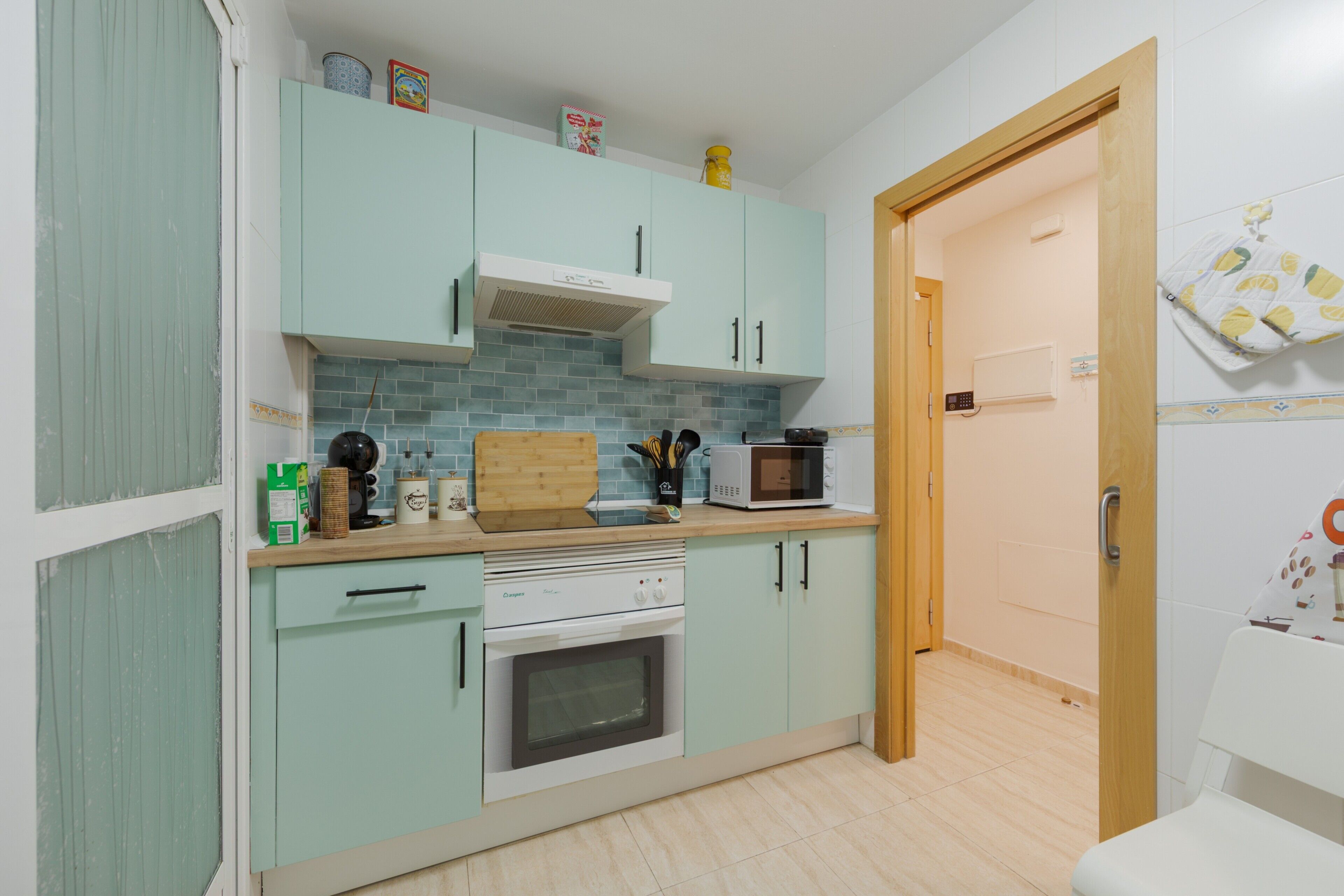 A kitchen with light blue cabinets, a microwave, a stove, and a wooden cutting board.