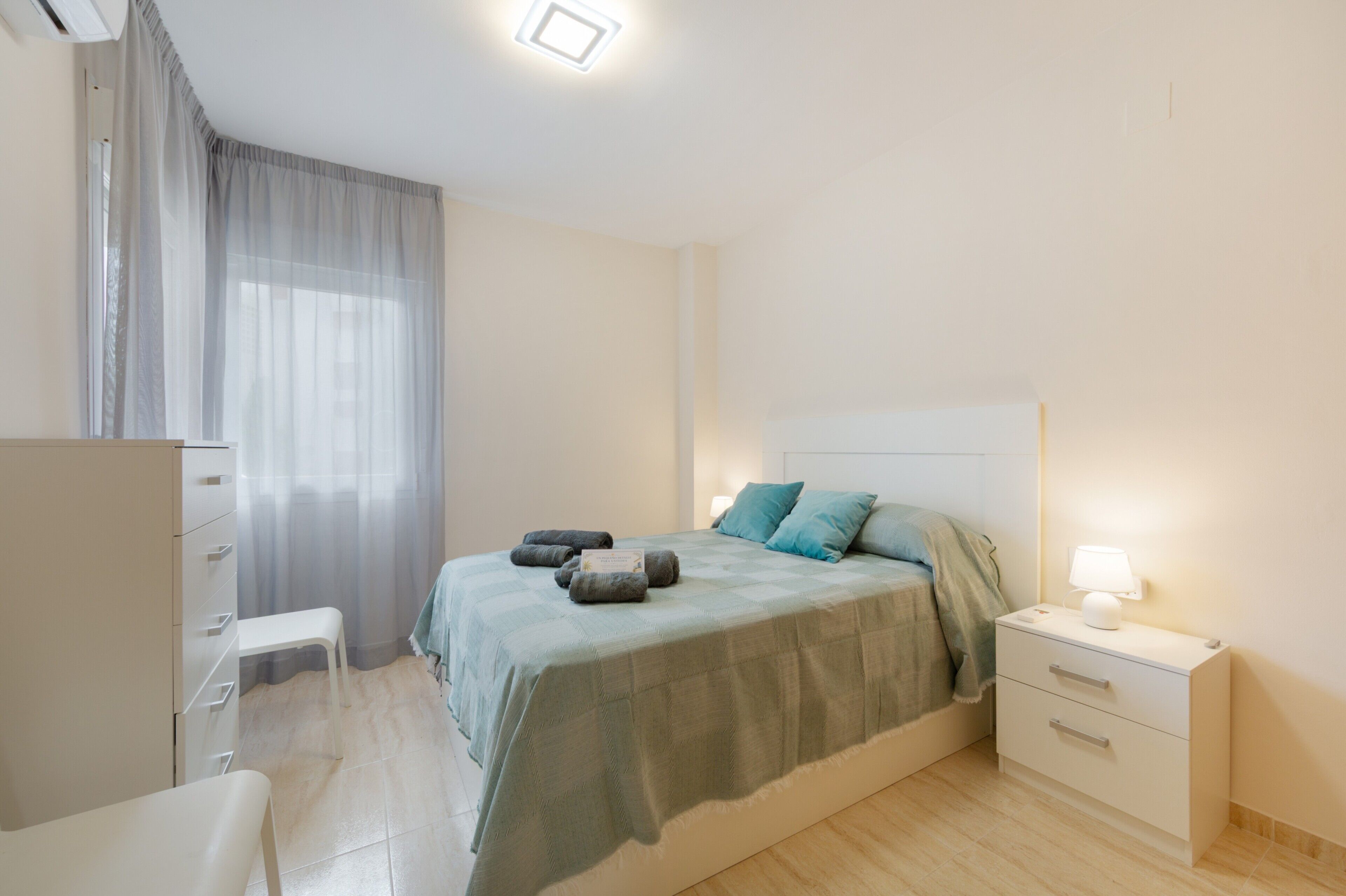 A bedroom with a bed, bedside table, lamp, and a chair.
