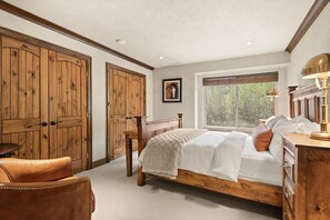A bedroom with a wooden bed, a wooden wardrobe, a leather chair, and a window with a view of greenery. - Spacious Retreat in Snowmass Village! Gas Fireplace, HT, on Free Shuttle (Snowmass Village)