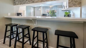 Uma cozinha com painel de backsplash de pedra, bancadas brancas e três banquetas pretas.