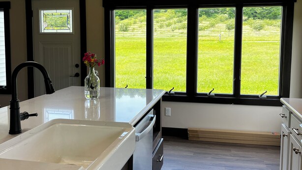 A kitchen with a large window, wooden beams, a sink, and a vase with flowers. - Charming 3-bedroom House on a Cherry Orchard (Suttons Bay)