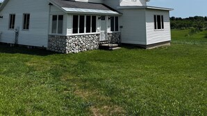 A two-story house with a stone foundation, a porch, and a grassy yard. - Charming 3-bedroom House on a Cherry Orchard (Suttons Bay)