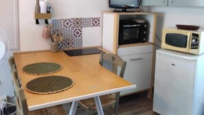 Pieni, käytännöllinen keittiö, jossa on puinen pöytä, tuolit, televisio, mikroaaltouuni ja kaapit.