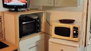 Kompakti keittiö, jossa on mikroaaltouuni, pieni jääkaappi, televisio ja kaappi.