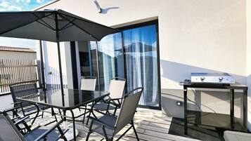 Une terrasse extérieure avec une table en verre, des chaises, un barbecue et une porte-fenêtre coulissante.