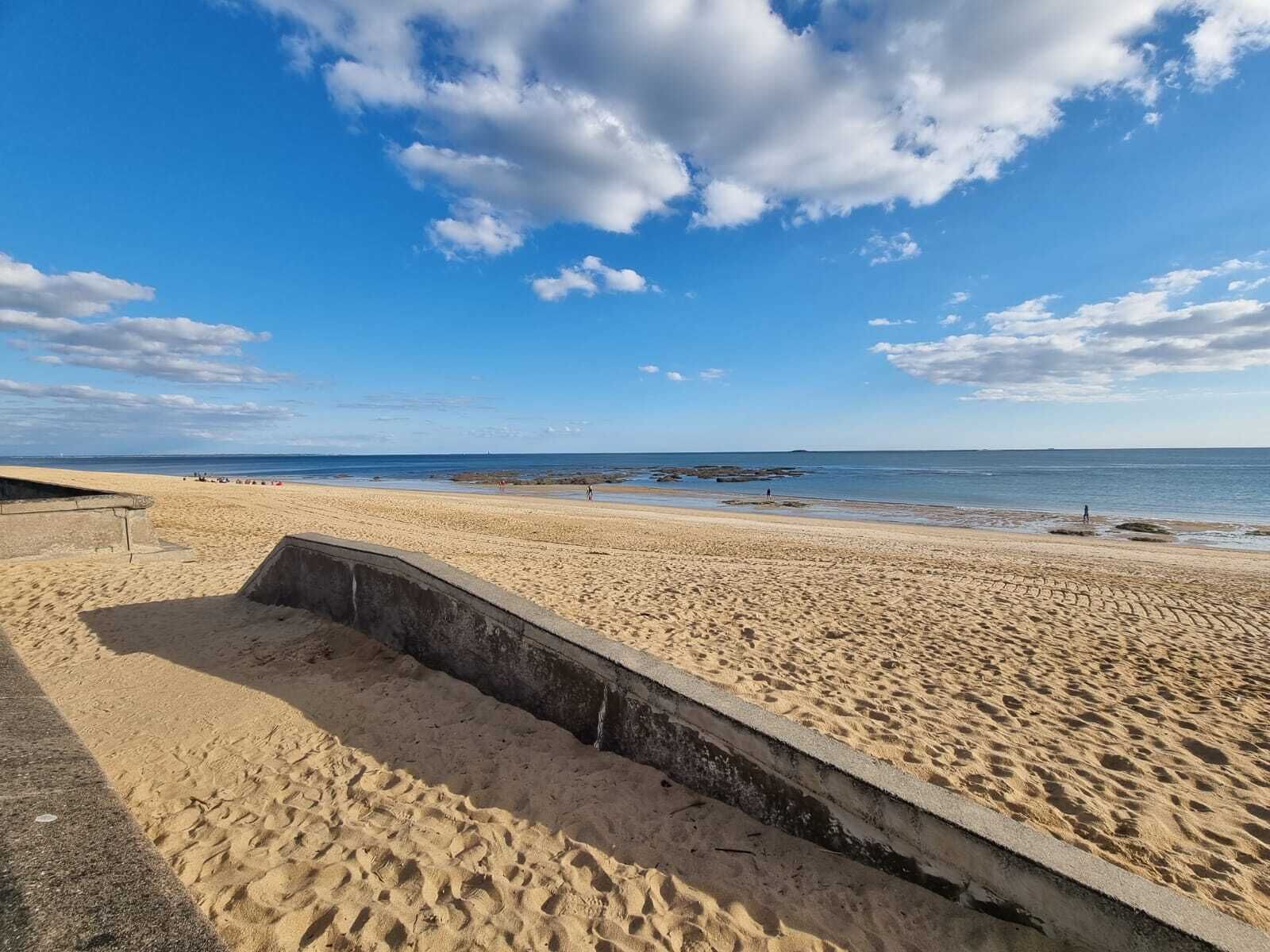 A sandy beach with a concrete structure, a clear sky, and calm water.