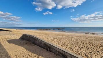 A sandy beach with a concrete structure, a clear sky, and calm water.