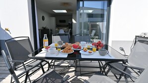 Taula de dinar amb menjar per esmorzar i cadires, una porta de vidre que dona a una cuina, i vista al cel.