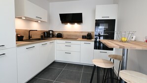 Una cuina moderna amb armaris blancs, taulell de fusta, forn de sobre i zona de bar amb tamborets.