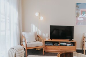 Een woonkamer met een televisie, een houten dressoir en een fauteuil.