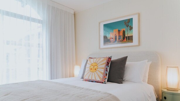 Ein Hotelzimmer mit einem Bett, einem Nachttisch, einer Lampe, einem Bild an der Wand und einem Fenster mit Vorhängen.