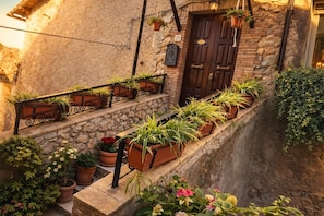 A stone building with a wooden door, potted plants on the steps, and a small sign above the door. - A cozy single-family home in the center of Tolfa. Pets allowed. (Tolfa)
