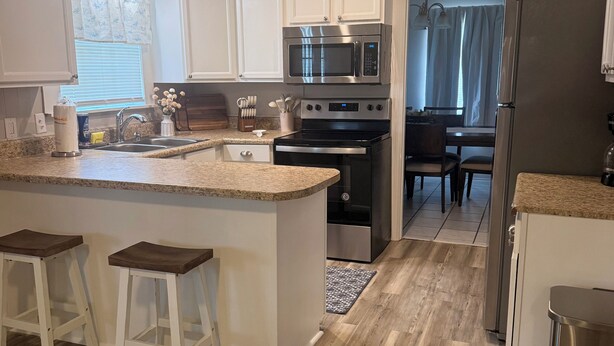 A modern kitchen with white cabinetry, stainless steel appliances, and a wooden floor. - Home Sweet Home Nearby Beach & MS Gulf Coast! (Grand Bay)