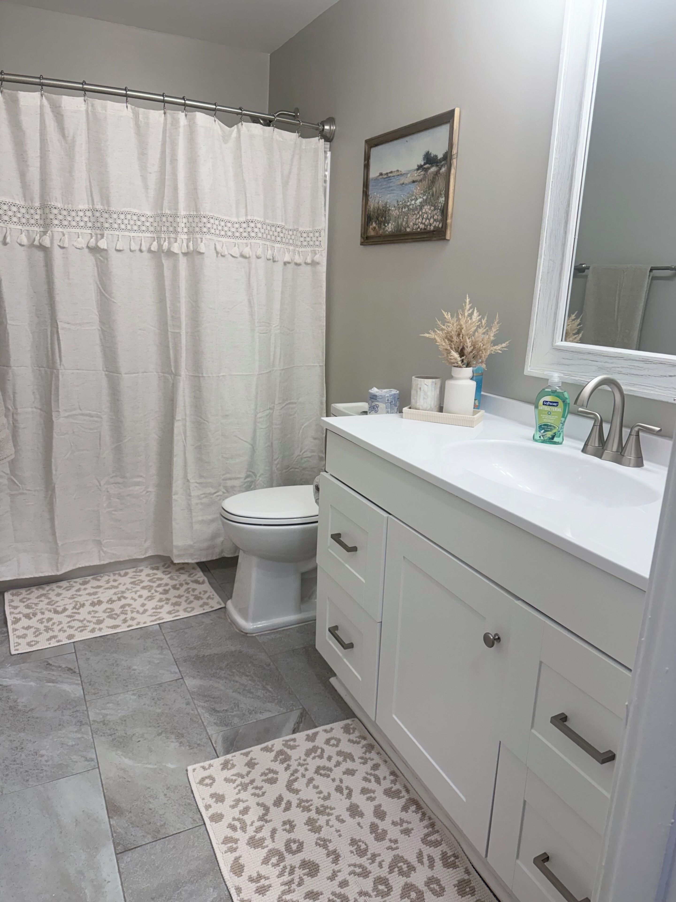 Un baño con inodoro, lavamanos con espejo, cortina de ducha y una pequeña planta en maceta.