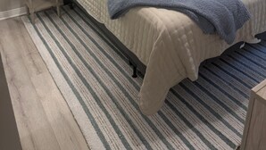 A bedroom with a bed, two bedside tables with lamps, a headboard, a window with curtains, and a striped rug. - Home Sweet Home Nearby Beach & MS Gulf Coast! (Grand Bay)