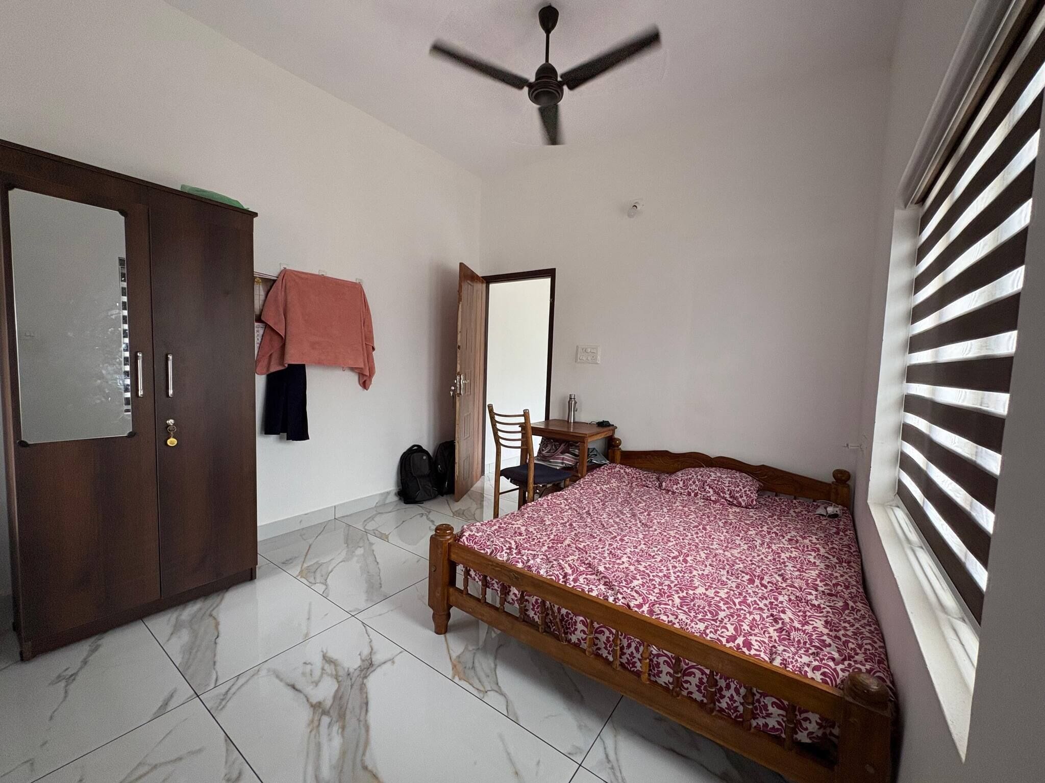 A bedroom with a bed, a desk, a chair, a wardrobe, and a ceiling fan.