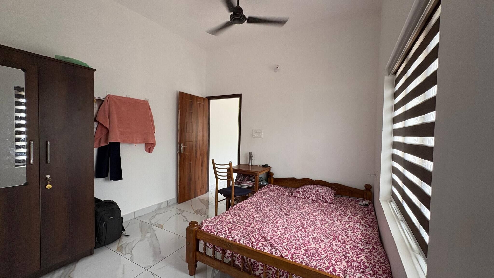 A bedroom with a bed, a desk, a chair, a wardrobe, and a ceiling fan.