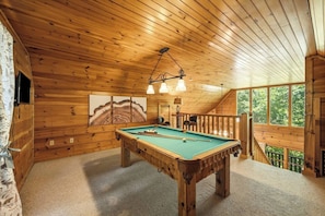A wooden interior with a pool table, artwork, and a balcony with a railing. - Peaceful Log Cabin Retreat with Hot Tub (Sevierville)