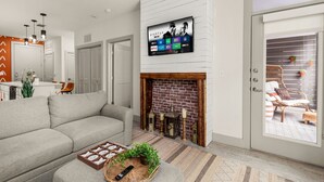 Una sala de estar moderna con un televisor de pantalla plana sobre una chimenea de ladrillo, un sofá gris y una mesa de centro de mimbre con un control remoto y objetos decorativos.