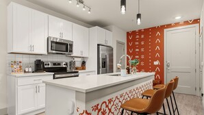 Una cocina moderna con armarios blancos, electrodomésticos de acero inoxidable y una isla central con taburetes de bar.