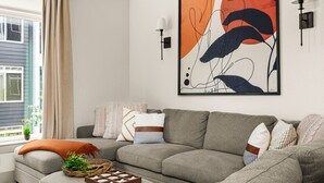 Una sala de estar moderna con un sofá seccional gris, un cuadro abstracto grande y dos lámparas fijadas a la pared.