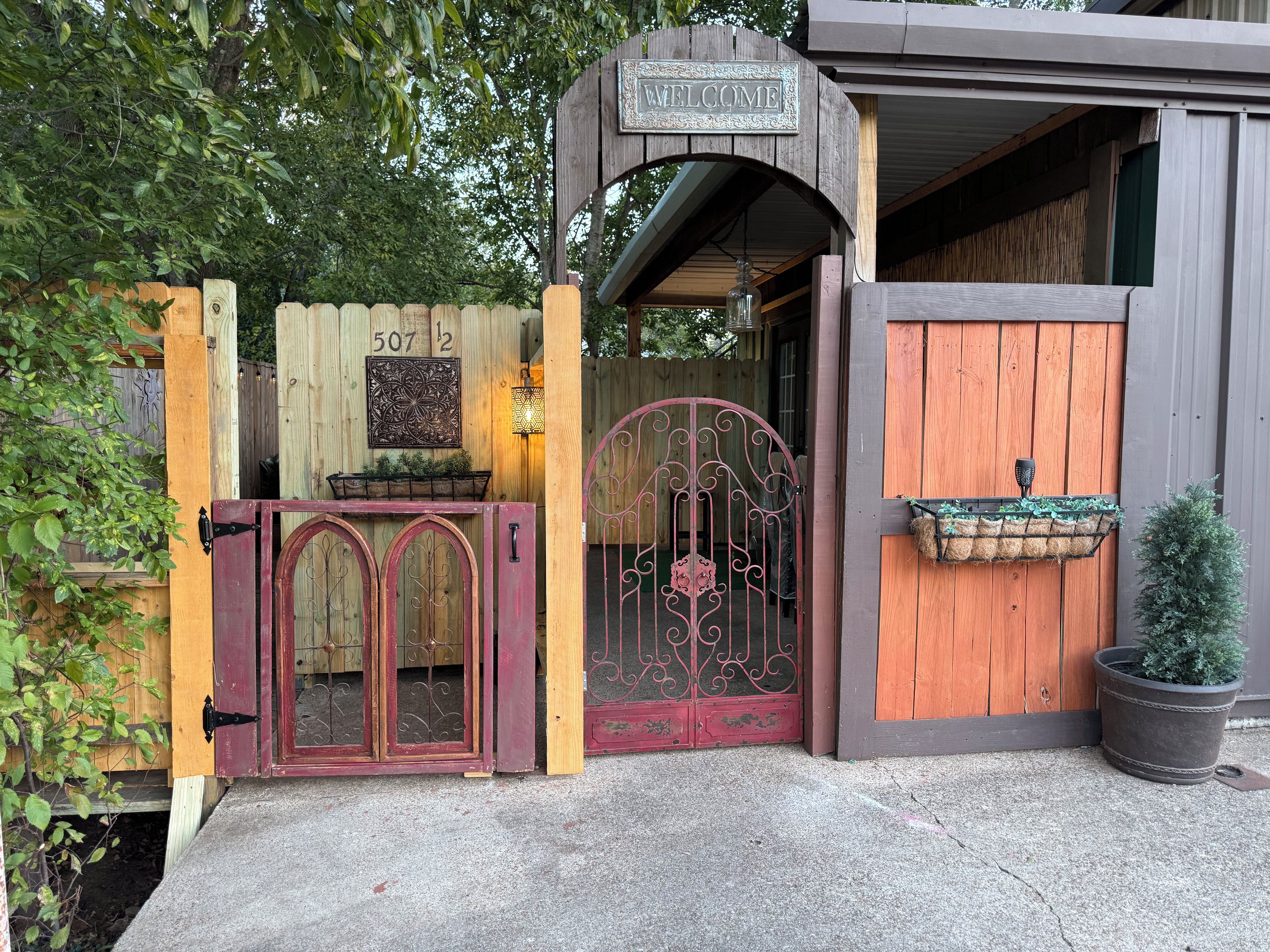 Une porte en bois avec une pancarte indiquant « BIENVENUE », une plaque portant un numéro et un pot de fleurs.