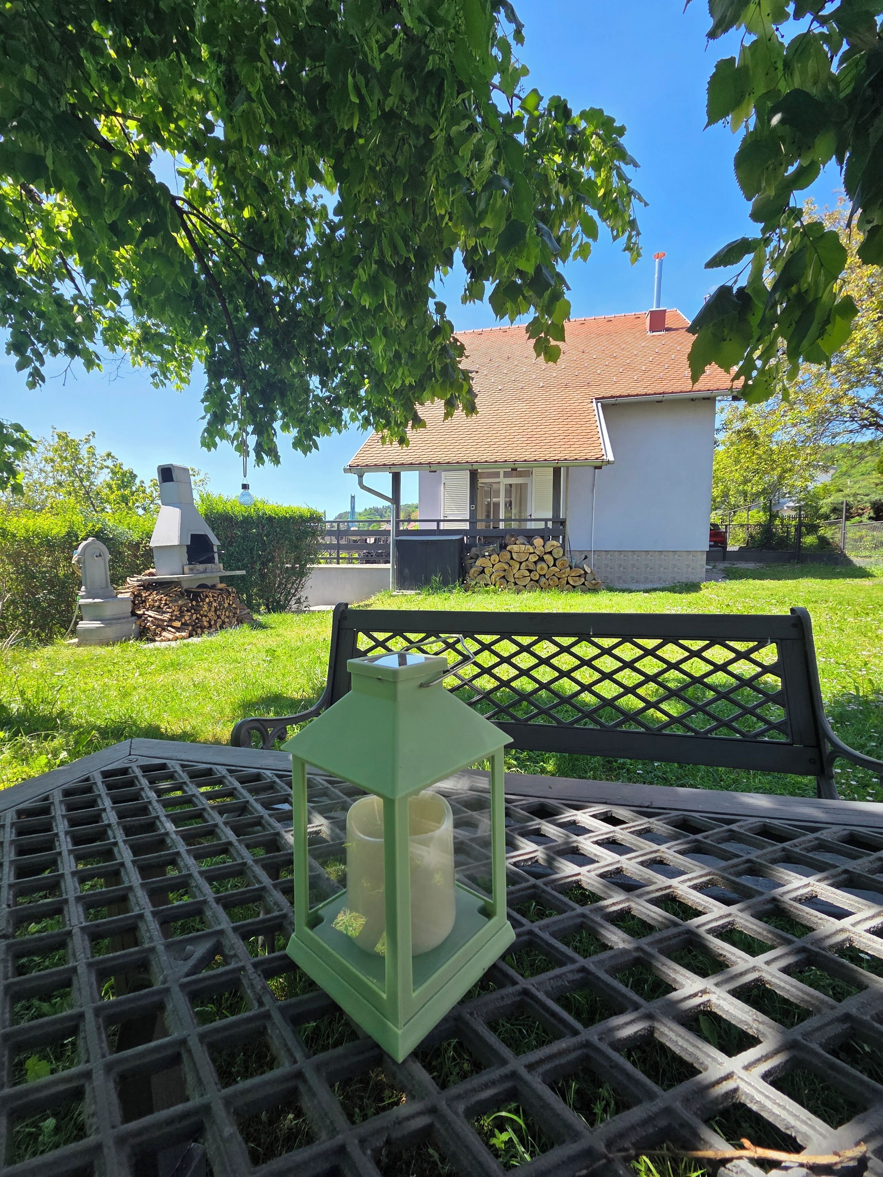Een terras met een groene lantaarn, een barbecue en een huis op de achtergrond.