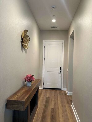 A hallway with a wooden bench, a white door, and a wall-mounted decorative piece. - 4BR Home: Theme Parks & Huntington Beach Nearby (Garden Grove)
