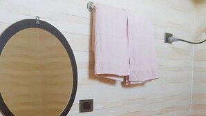 Un bany amb un lavabo blanc, un mirall rodó, un penjador de tovalloles amb una tovallola rosa i un recipient verd a la paret.