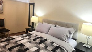 A hotel room with a bed, two bedside tables, a nightstand, a lamp, and a mirror.