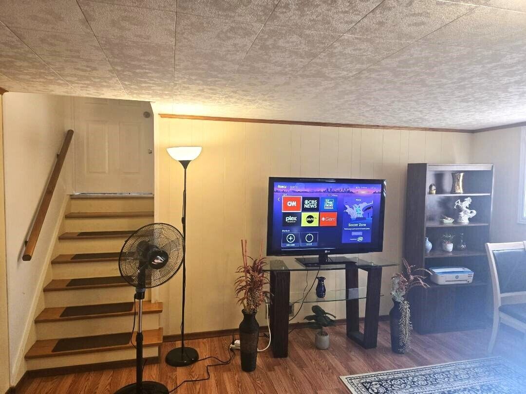 A living room with a TV, a fan, a staircase, and a bookshelf.