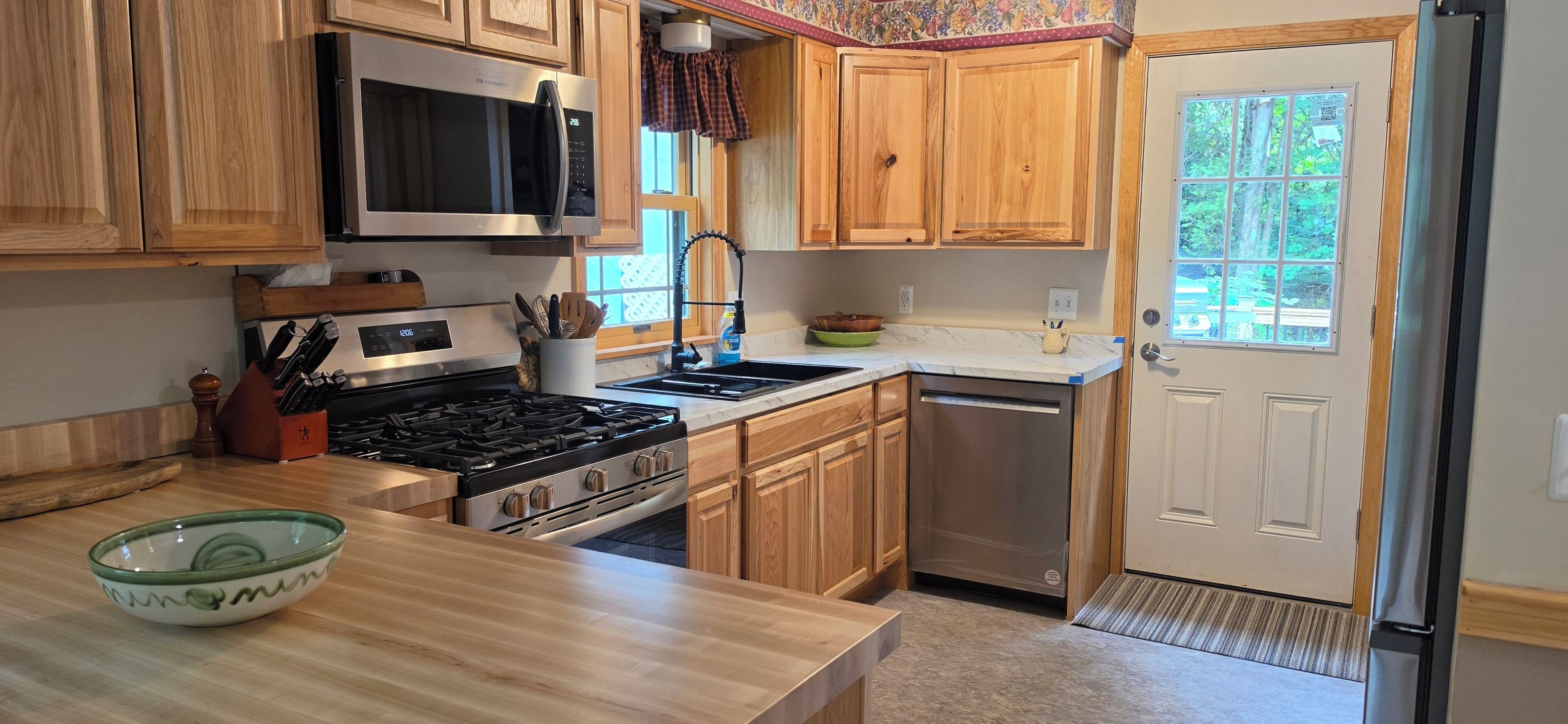Una cocina con armarios de madera, microondas, estufa, fregadero y refrigerador.