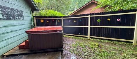 Un patio trasero con jacuzzi, terraza de madera y valla decorativa.